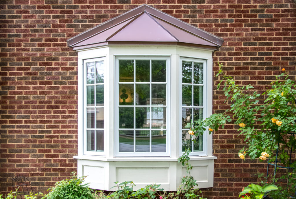 Bay window with copper roof on traditional brick home with flowers below